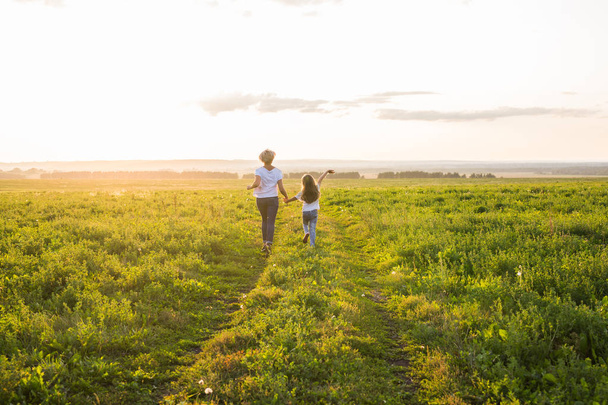 vue arrière de la mère et de la fille courant dans un champ vert avec coucher de soleil sur le fond
 - Photo, image