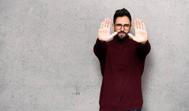Handsome man with glasses making stop gesture for disappointed with an opinion over textured wall - 写真・画像
