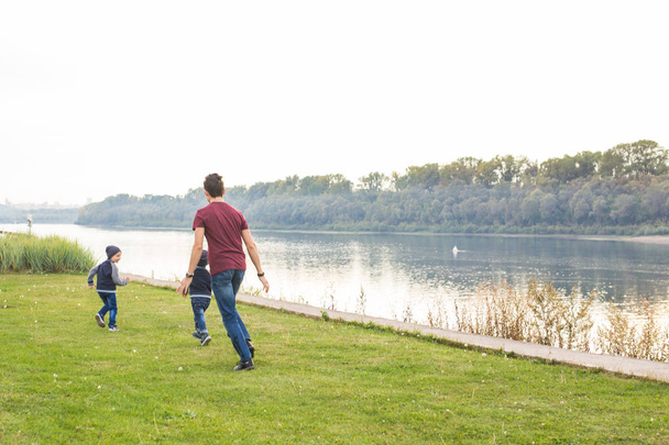 Dzieciństwo, pojęcie rodziny - ojciec, grając z dwóch synów, w pobliżu jeziora - Zdjęcie, obraz