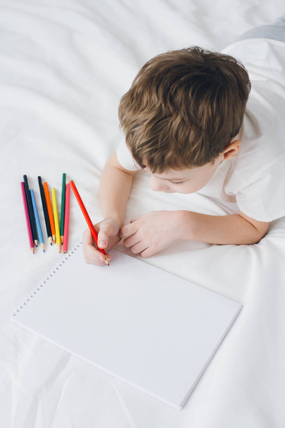 Boy draws with colorful pencils sitting on the bed  - Fotografie, Obrázek