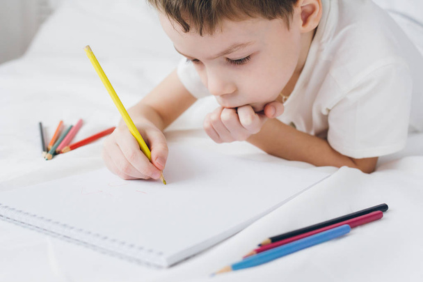 Boy draws with colorful pencils sitting on the bed  - Photo, image
