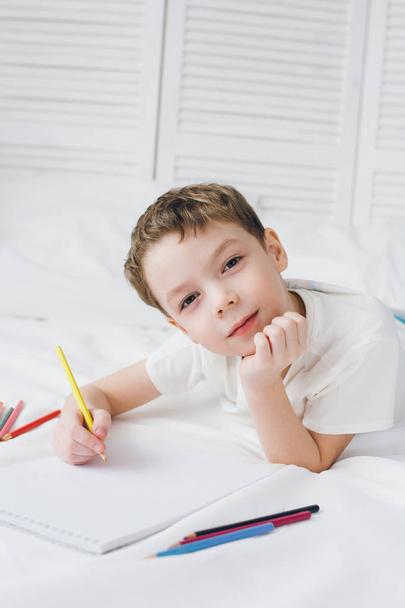 Boy draws with colorful pencils sitting on the bed  - Фото, зображення