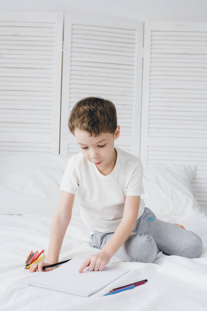 Poika kiinnittää värikkäitä kyniä istuu sängyllä
  - Valokuva, kuva