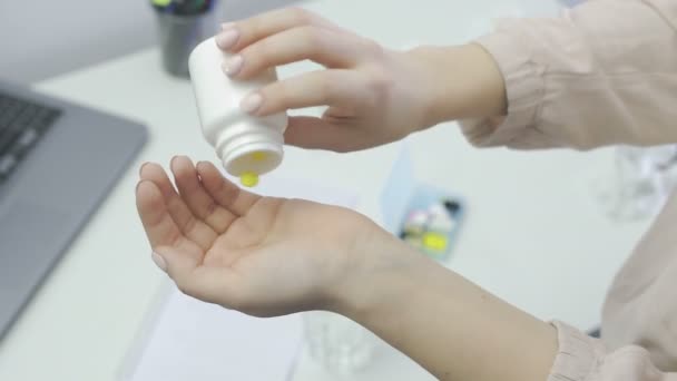 Woman pours two a yellow pills out of the bottle, take it and drink water - Imágenes, Vídeo