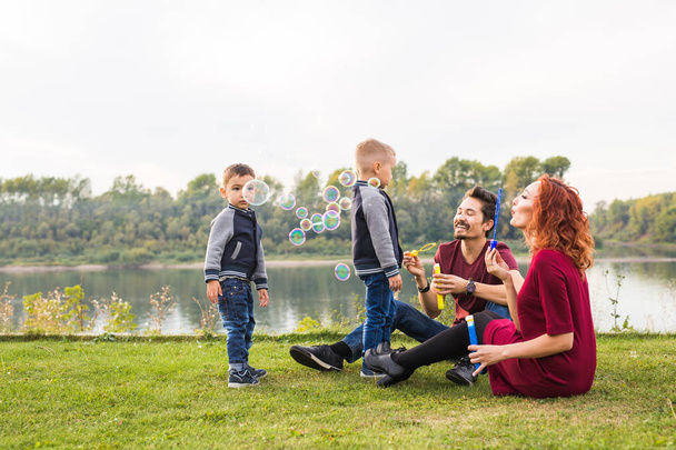 Concepto de familia y naturaleza - Madre, padre y sus hijos jugando con burbujas de jabón de colores
 - Foto, Imagen