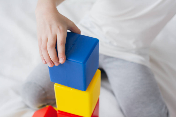 Boy plays and builds a tower of colorful plastic cubes  - Fotó, kép