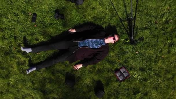 homem deitado na grama cercado por um tripé, flashes e mochilas
 - Filmagem, Vídeo