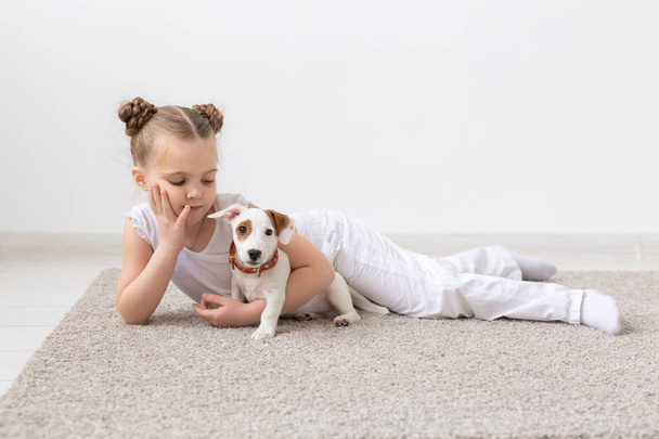 concepto de la infancia, mascotas y perros - Niña posando en el suelo con el cachorro
 - Foto, Imagen