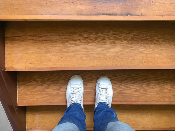 Hombre con jeans azules y zapatos blancos en una escalera de madera
 - Foto, imagen