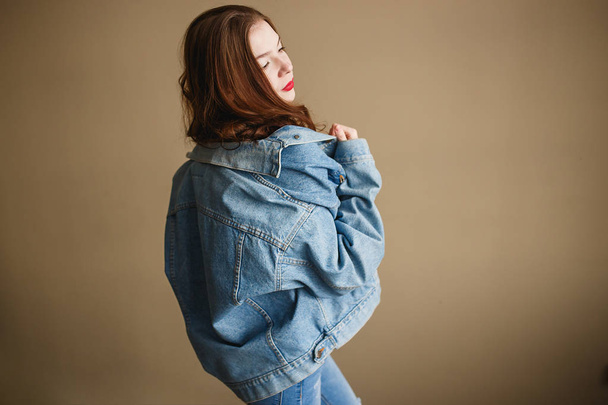 Young Female Model Posing in Denim Jacket on Beige Background. Back to 1990s Fashion Lifestyle Style Concept - Fotó, kép