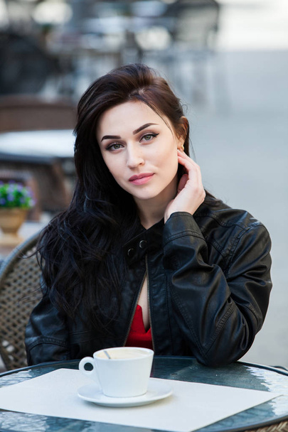 Outdoors fashion portrait of young beautiful girl drinking coffee.Close up portrait of a smiling young girl holding take away coffee cup outdoors.Young stylish woman drinking coffee in a city street  - Фото, зображення