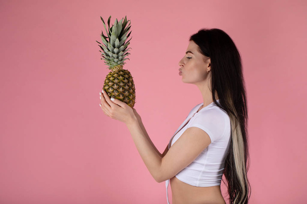 beautiful sexy young girl standing on a pink background with pineapple. - Foto, afbeelding
