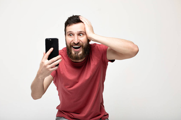Portrait of a cheerful young man wearing casual clothes standing isolated over grey background, using mobile phone. - Φωτογραφία, εικόνα