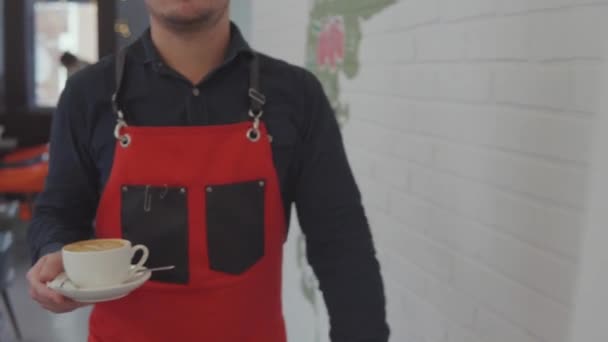 Adult male waiter is bringing coffee cup to male visitor in cafe - Footage, Video