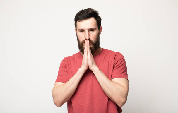 Picture of young guy dressed casually isolated on grey background, having put hands together in prayer or meditation, looking relaxed and calm, dreaming and waiting for all best - Fotografie, Obrázek