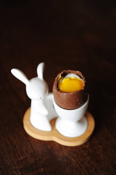 Πασχαλινό αυγό επιδόρπιο σοκολάτας με κρέμα μίμηση του λευκού και του κρόκου. Ο κάτοχος με λαγουδάκι. Ξύλινο υπόβαθρο, ελεύθερο χώρο - Φωτογραφία, εικόνα