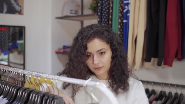 Frau kauft in Bekleidungsgeschäft in Einkaufszentrum ein und nimmt Kleiderbügel aus Regal - Filmmaterial, Video