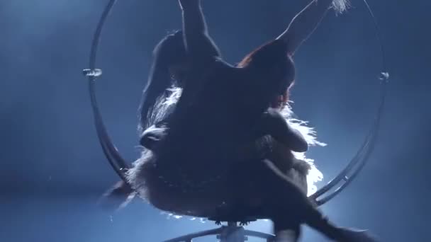 Female balancer in beige leotard back lying hang on aerial hoop on black background. Silhouette. Slow motion. Close up - Felvétel, videó