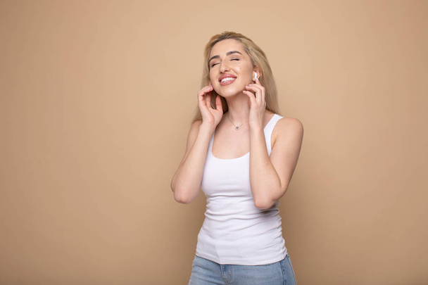 Portrait of a cheerful young woman in headphones listening to music isolated over beige background - 写真・画像