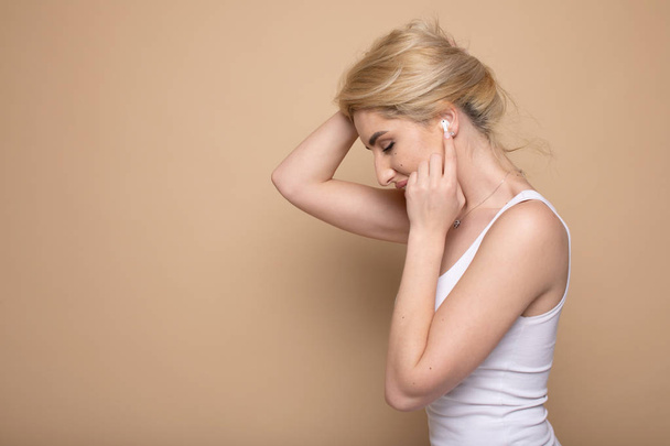 Πορτραίτο μιας εύθυμη νεαρής γυναίκας στα ακουστικά ακούγοντας μουσική απομονωμένη σε μπεζ φόντο - Φωτογραφία, εικόνα