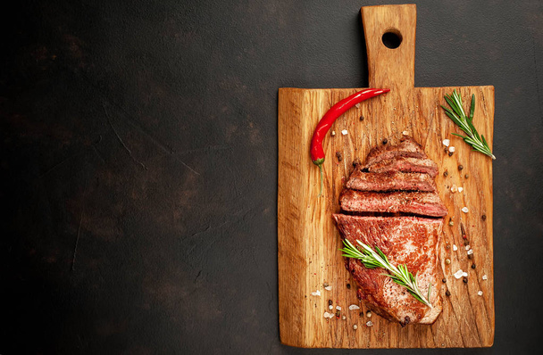 Ready-to-eat New York black angus steak with ingredients on a cutting board. Ready meal for dinner on a dark stone background. with copy space - Photo, Image