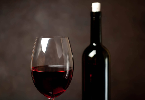 Wine glass with red wine and bottle against a stone background.  - 写真・画像