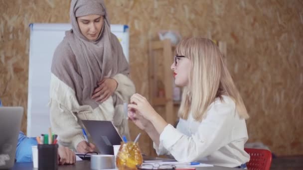 blonde Frau spricht im Büro, muslimisches Mädchen macht Notiz, Mann hört zu - Filmmaterial, Video