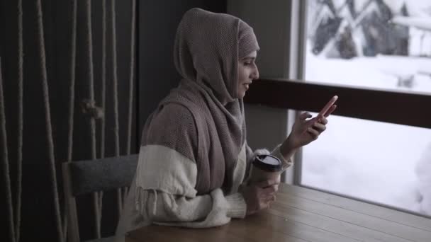 Αραβική γυναίκα παρακολουθεί βίντεο και εικόνα στο smartphone κάθεται στο καφέ - Πλάνα, βίντεο