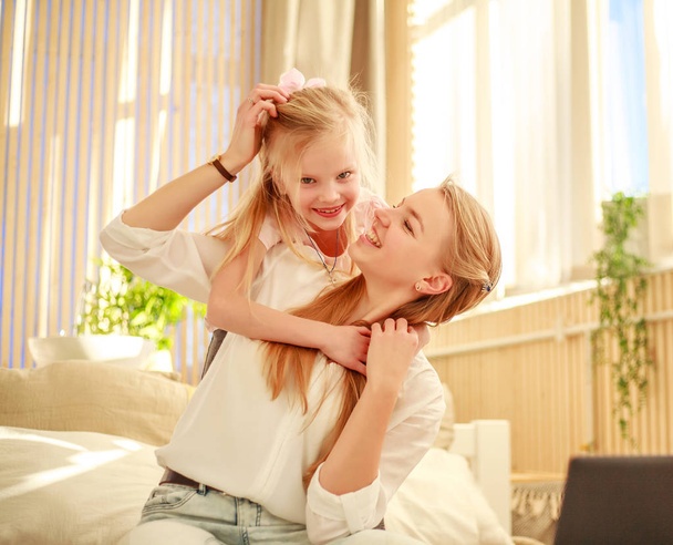 Mother and daughter joyfully hugging at home on bed - Photo, Image