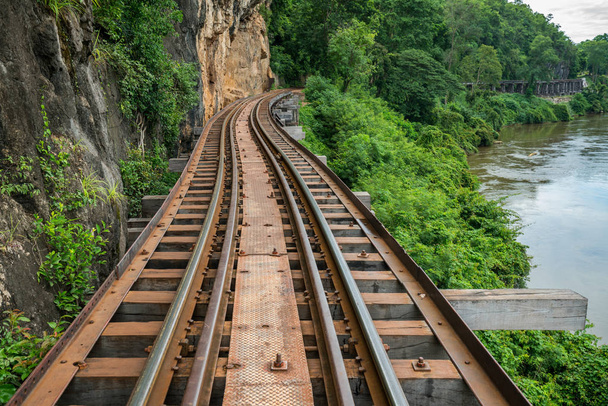 Old railroad tracks on bridge beside cliff rock - Фото, изображение