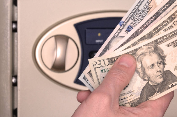 Male hand with US dollars on the background of the safe with the door open. The concept of saving money, service in a hotel or bank, storage of banknotes in a box with a code number. - Photo, Image