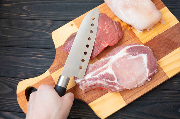 Variety of raw meat beef meat on bone, pork meat and chicken fillet on wooden background with butcher knife, top view - Photo, Image