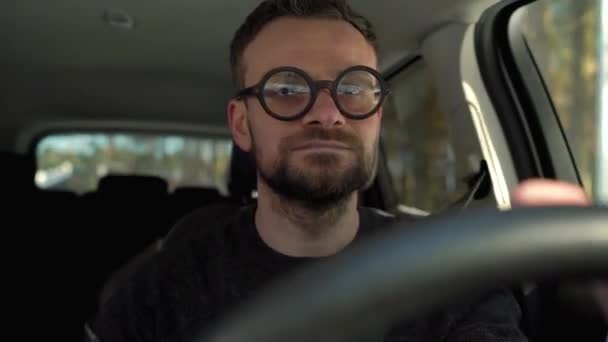 Задоволений бородатий чоловік в окулярах водить машину по вулиці в сонячну погоду
 - Кадри, відео