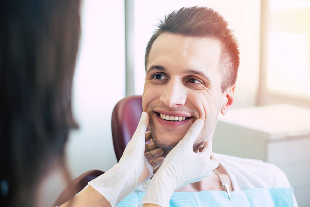 Un sourire éblouissant. Un homme dans une chaise dentaire devant un médecin qui surplombe son travail professionnel fait il y a plusieurs jours et le visage des hommes montre que le travail est parfait
. - Photo, image