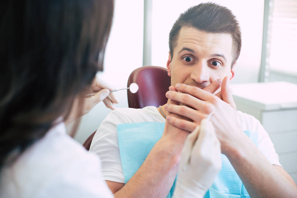 Its plain scary! A dentist is trying to give a treatment to a man but she cant because he is extremely scared and shows it with his hands over his mouth and a look on the instruments. - Photo, image