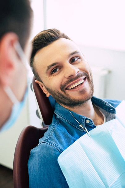 Pretty face mimic and a white smile of a nice man in a dental chair after getting a doctors treatment  in a professional clinic. - Foto, imagen