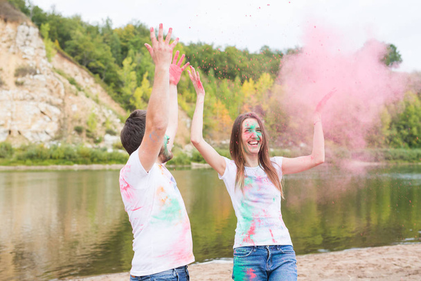Festival holi, holidays, tourism and nature concept - Couple dressed in white shirts playing with colorful dust - Foto, Imagem