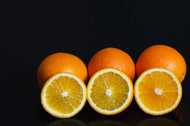 Halved and whole oranges over black background, side view. Space for text. - Photo, Image