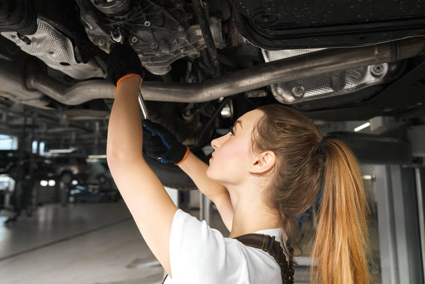 Girl working undercarriage of automobile, using tool. - 写真・画像