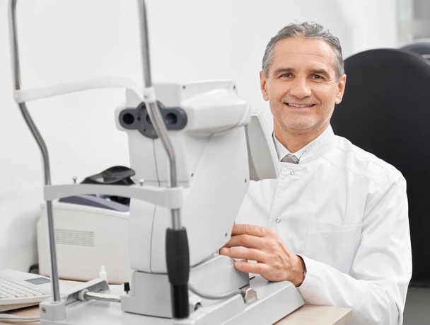 Experienced doctor ophthalmologist posing with slit lamp. - 写真・画像