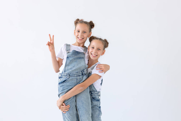 Familien- und Liebeskonzept - zwei lächelnde Zwillingsschwestern, die sich vor weißem Hintergrund umarmen - Foto, Bild
