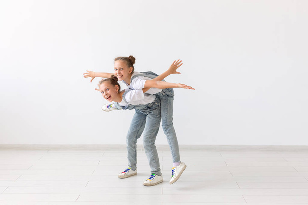 personas, niños y concepto familiar - niña llevando a su hermana gemela a cuestas sobre fondo blanco
 - Foto, Imagen