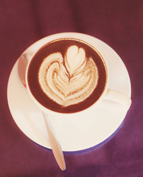 Warme Cappuccino koffie gedecoreerd met bloeiende bloem schuim kunst op gestoomde melk schuim in witte cup op houten tafel achtergrond. Espresso koffie drinken, drank, 's Middags drinken en cafeïne Concept gebaseerd - Foto, afbeelding