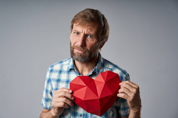 Unhappy mature man in checkered shirt holding heart shape - Foto, Imagen