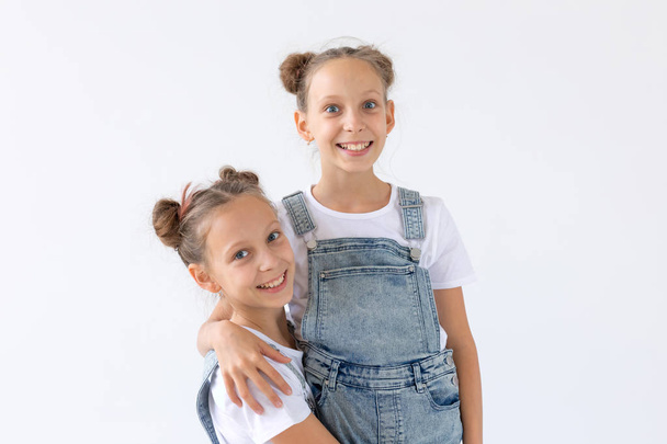 Concepto de familia y amor: dos hermanas gemelas sonrientes abrazándose sobre un fondo blanco
 - Foto, imagen