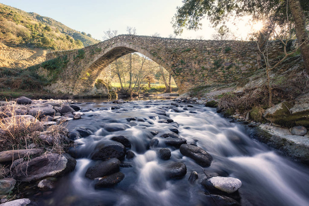 Ponte de pedra antiga sobre o rio que flui na Córsega
 - Foto, Imagem