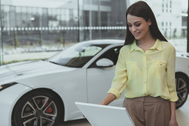 Elegant young woman buying new car at dealership - 写真・画像