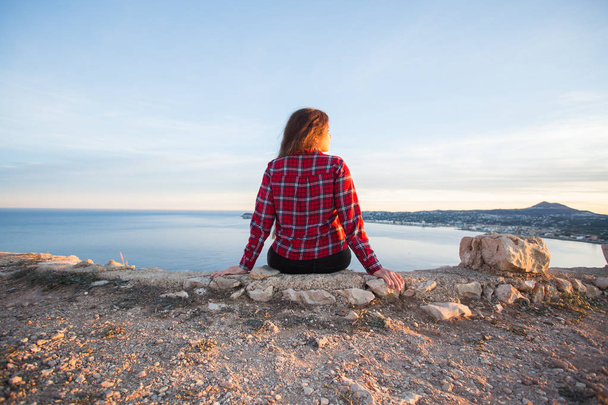 Podróży, przygody i pojęcie samotności - dziewczyna siedzi na skraju urwiska i patrząc na morze - Zdjęcie, obraz