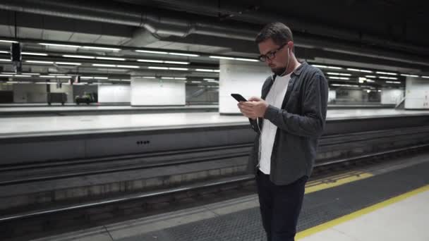 El hombre está parado cerca del tren subterráneo y esperando, usando auriculares
 - Metraje, vídeo