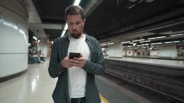 Townsman se dívá na obrazovku mobilního telefonu na stanici metra - Záběry, video